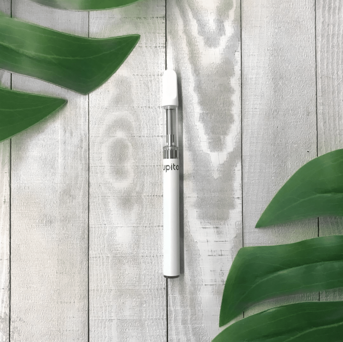 Jupiter CCELL® Liquid6 Standard Vaporizer Laying on White Wood Table with Tropical Leaves